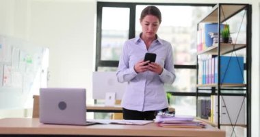 Düşünceli iş kadını yönetici ofise girdi, akıllı telefon ekranına baktı ve masaya çarptı. Akıllı telefon bağımlılığı kavramı