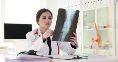 Düşünceli kadın doktor klinikte diz eklemi röntgeni sonuçlarını inceliyor. Diz yaralanması tedaviye neden olur