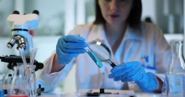 Bilim adamı tüpteki mavi sıvıyı büyüteçle inceliyor. Laboratuvarda zehirli organik çözücüler.