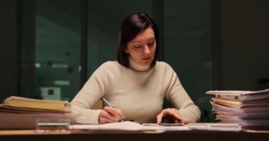 Ofiste geç saatlere kadar çalışan ve telefona bakan yorgun bir iş kadını. Gece geç saatlerde ofiste rapor yazmaktan yorgun düşmüş.