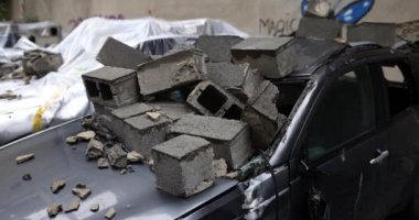 Siyah otomobilin çatısı sayısız kayanın çarpmasıyla hasar gördü. Ağır çekimde parçalanmış aracın parke taşları nokta yüzeyi