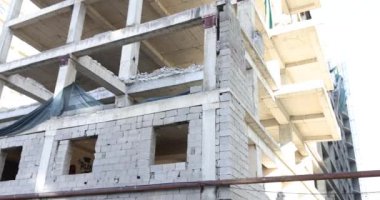 İnşaat halindeki bina iskelet iskeleti ile ayakta duruyor. Güneş kısmen tamamlanmış yapıda uzun gölgeler bırakır. İlerlemenin sembolü