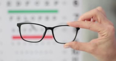 Kadın doktor hastanede Snellen dosyasına karşı elinde gözlük tutuyor. Kadın çerçeveleri ve lensleri değerlendirir ve hastanın özel ihtiyaçlarını karşılar