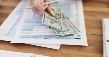 Kadın girişimci masadaki doldurulmuş vergi formuna dolar banknotları koyar. İş kadını şirket ofisinde vergilendirme parası sayar