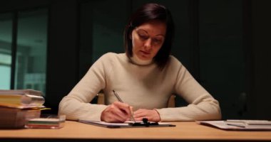 Odaklanmış bir kadın iş yerinde oturur ve akşamki toplantı için konuşma hazırlar. Sorumlu işçi kılavuz sunumuna özenle özet yazar