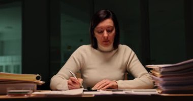 Sorumlu kadın işçi gece iş yerindeki raporları kontrol ediyor. Aşırı çalışan esmer kadın, geç saatlere kadar iş yerinde kalan telefonla bakıyor.