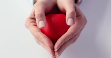 Kadın beyaz arka planda kalp oyuncağını göstererek ellerini açıyor. Kadın, sevgi ve şefkat ile ilgili mesajı iletiyor ve olumlu bağlantıyı teşvik ediyor