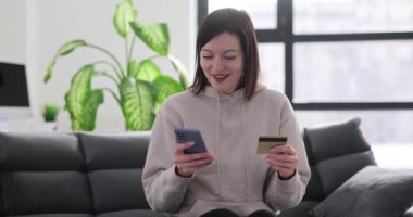 Gülümseyen kadın internetten kredi kartı ve akıllı telefonuyla mal alıyor. Esmer kadın evde alışveriş yapmak için bankacılık hizmetlerini kullanıyor.