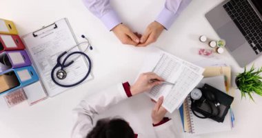 Kadın doktor, masasında oturan erkek hastaya kan testinin sonuçlarını açıklıyor. Profesyonel, sağlık durumunun ayrıntılı bir açıklamasını sunar