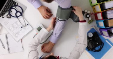 Kadın doktor, hastayı tansiyon ölçüm prosedürüne hazırlayan lastik kelepçeleri yerleştirir. Adam özel klinikte muayene oluyor.