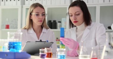 Bayan bilim adamı kimya laboratuarında asistan notları incelerken gösterge kağıdını sıvıya koyar. Kadın kimyagerler klinikte sıvı testi yapıyorlar.