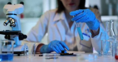 Laboratuvar asistanı, test tüpünü iş yerinde mavi sıvıyla değiştiriyor. Kadın kimyager tıp laboratuarında renk sıvısı maddesiyle çalışıyor. Bilim teknolojisi