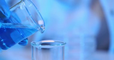 Araştırmacı tıp laboratuarındaki deney şişesinden mavi sıvı boşaltıyor. Bilim adamı kimyasal laboratuvarda sıvı maddeleri yavaş çekimde birleştiriyor. Madde testleri