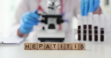 Minyatür tahta küpler masada HEPATITIS 'i oluşturur. Doktor, mikroskop yavaş çekim kullanarak hepatit için kan örneklerini analiz ediyor.