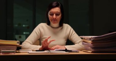 Şirket çalışanı iş yerindeki parmaklarını kağıtlarla tıkırdatıyor. Kadın çalışan, gece yorgunluğunu gösteren akıllı telefondan saati kontrol ediyor.