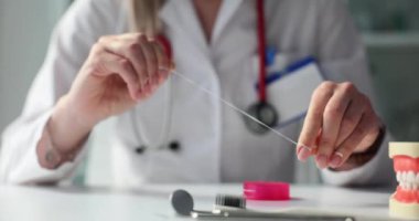 Hijyenist kadın masadaki parmaklarına diş ipi takıyor. Dişçi klinikte kişisel ağız temizliği konusunda rehberlik eder. Stomatolog muayenesi