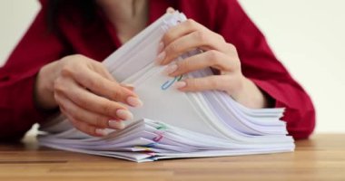 Kadın işçi, ofiste klipslerle tutturulmuş kağıt yığınını inceliyor. Evrak işleri arasında iş anlaşmasını kolaylaştırmaya adanmışlığın yansıması
