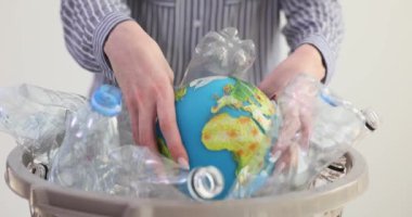 Bayan plastik şişelerle dolu sepetten küre topluyor. Plastik kirliliğinin gezegen üzerindeki zararlı etkilerinin giderilmesi