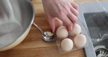 Önlüklü kadın aşçı yumurtaları çatlaklar ya da kusurlar için inceliyor. Kahvaltı hazırlıkları için mutfak masasında duran yumurtalı plastik kap.