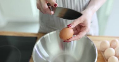 Önlüklü genç kadın şef keskin bir bıçakla yumurta kabuğunu kırıyor. Dişi, omleti yavaş çekimde yapmaya başlamak için yumurtayı kaseye kırar.