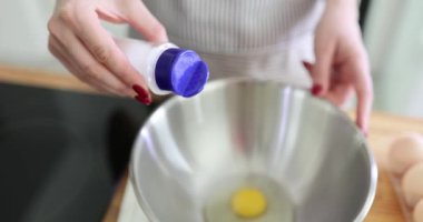 Genç kadın şef yumurtaya bir tutam tuz ekler. Önlüklü kadın mutfakta duruyor ve tuz karıştırıcı kullanarak tuz ekliyor.