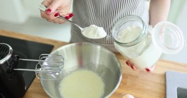 Genç ev hanımı çırpılmış yumurta ve süte dikkatle un ekler. Kadın lezzetli krepleri ağır çekimde yapmak için gerekli malzemeleri karıştırıyor.