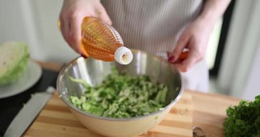 Genç kadın aşçı lahana salatasına ayçiçeği yağı döküyor. Önlüklü ev hanımı, yavaş çekimde yağ ekleyerek sebze salatasının tadını artırır.