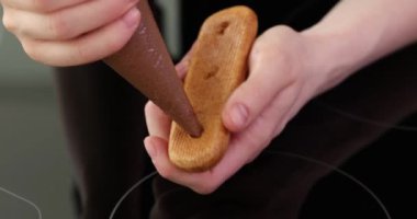 Aşçı, pasta poşeti kullanarak çikolatalı kremayı ekine sokuyor. Deneyimli aşçı modern mutfaktaki misafirler için lezzetli bir tatlı hazırlar.
