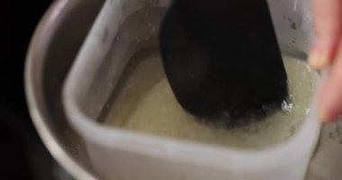 Şekerleme malzemelerini mutfakta bain-marie metoduyla eritiyor. Aşçı spatula kullanarak tereyağlı şekeri karıştırır ve pürüzsüz bir tutarlılık sağlar.