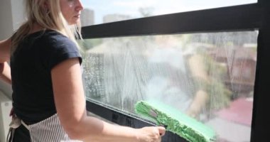 Kadın dikkatlice cam yüzeyinin her santimini paspasla siliyor. Genç ev hanımı her paspas geçişinde cam temizliği ve berraklığı sağlar.
