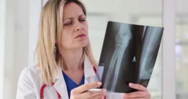 Kadın doktor, ağır çekimde kemiğin röntgen görüntüsünü inceliyor. Tıp çalışanı odaklı ifade görevin ciddiyetini yansıtır