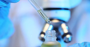 Laboratuvar çalışanı, modern mikroskoba karşı pipetle reaktörü şişeye damlatıyor. Eldivenli teknisyen yavaş çekim araştırmasına hazırlanıyor.