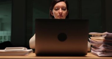 Şirket çalışanı şirket laptopunu iş yerinde ağır çekimde rahatlıkla kapatıyor. Yorgun kadın çalışanlar akşam raporlarını bitiriyor.