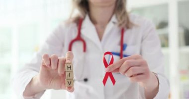 Doktorun elinde hastanede iş yerinde HIV virüsü taşıyan kırmızı kurdele ve tahta küpler var. Steteskoplu kadın terapist virüsü hatırlatıyor.