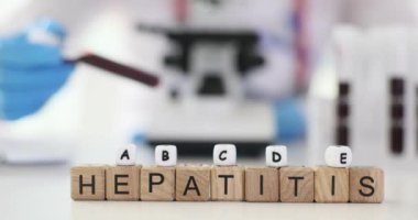 Minyatür tahta küpler masada HEPATITIS kelimesi oluşturur. Doktor çeşitli tip hepatit yavaş çekim için kan testi uygular.