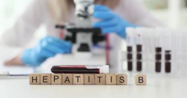 Minyatür tahta bloklar masanın üzerinde HEPATITIS B ifadesi oluşturur. Kadın doktor kan örneğini modern aletlerle inceliyor.