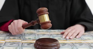 Yargıç tokmağı masasında dolarlarla kaplı otururken vurdu. Kadın dikkatli davranmayı emrediyor ve işlemlerin yavaş ilerlediğini gösteriyor.