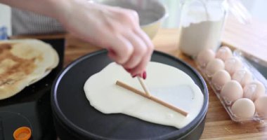 Kadın aşçı mutfakta spatulayla krep hamuru yayıyor. Ev hanımı modern aletlerde eşit derecede hamur işi üretiyor.