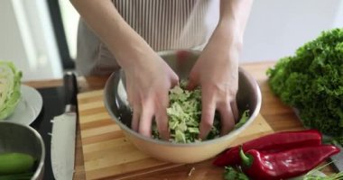 Kadın elleriyle doğranmış lahana ve salatalığı karıştırıyor. Ev hanımı besleyici salata yapmak için taze ve organik malzemeler kullanır.