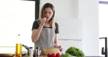 Kadın aşçı yemek pişirirken küçük bir parça salatalık tatmak için ara verir. Sebze için şefin takdir edilmesi doğal tat alma duyusuna derinlik katar.