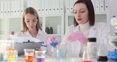 Laboratuvarda çalışan iki bilim adamı mataradaki mavi sıvıyı inceliyor. Bilimsel bir laboratuvarda ortak çalışma