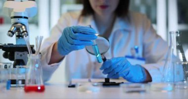 Bilim adamı deney tüpünü büyüteçle mavi sıvıyla inceliyor. Laboratuvar çalışanı yeni bir aşı ya da mavi zehirli çözücü araştırıyor.