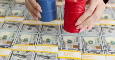 Yüz dolarlık banknotların arka planına karşı mavi ve kırmızı variller dolusu petrol. Petrol ürünlerinin maliyeti