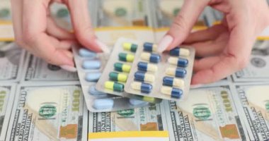 Amerikan dolarları ve tıbbi kapsüllerin arka planındaki haplar yakın plan. Uyuşturucu fiyatları ve sağlık hizmetleri için ilaç ticareti kavramı