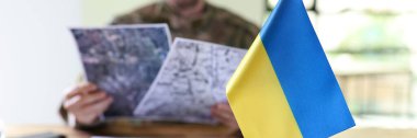 Ukraine flag in front of military man holding in hands secret plans of Ukrainian counteroffensive operation closeup. Intelligence service analysing war plans against Russia clipart