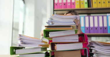 Kadın, ofisinde bir yığın dosya ile boğulmuş durumda ve çalar saati var. Çalışma konseptini düzenleme zorluğu