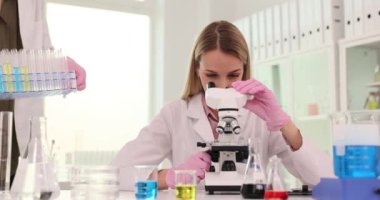 Kadın bilim adamı deney sırasında laboratuvarda mikroskop kullanır. Laboratuvar asistanı araştırma için test tüplerine sıvı koyuyor.