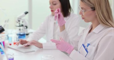 Modern bir laboratuvarda mavi sıvıyla çalışan iki bilim adamı. Laboratuvardaki test tüpüne mavi sıvı pipetler damlatın. Laboratuvarda alkol ve çözücü araştırması
