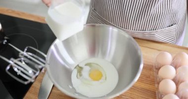 Kadın un ve yumurtalarla kaseye süt döker. Mutfakta hamur hazırlıyorum.