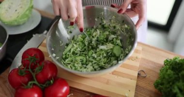 Kadın mutfaktaki bir kasede taze yeşil salata ve salatalık karıştırıyor. Taze sebze salatası hazırlıyorum.
